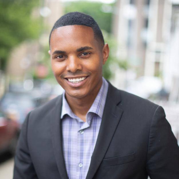 A man in a suit and plaid shirt is smiling for the camera.