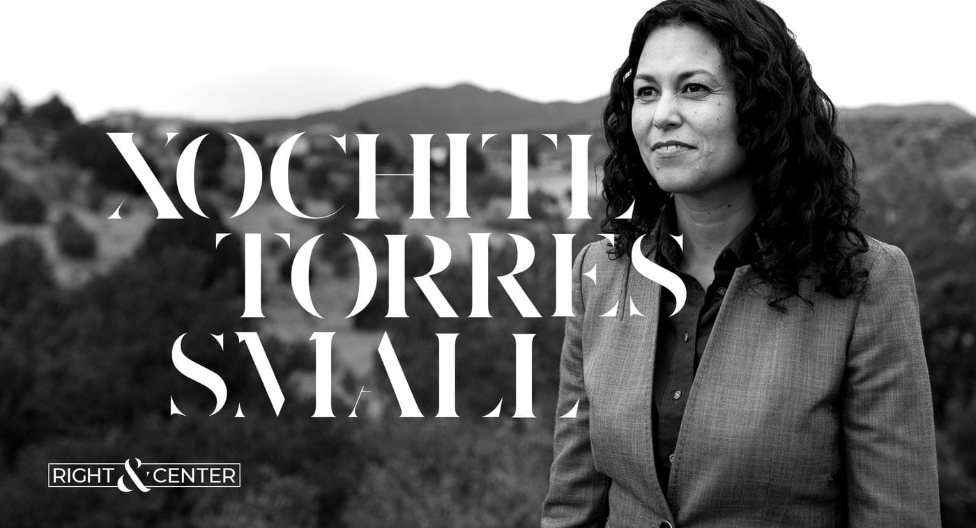 A woman in a suit is standing in front of a mountain.