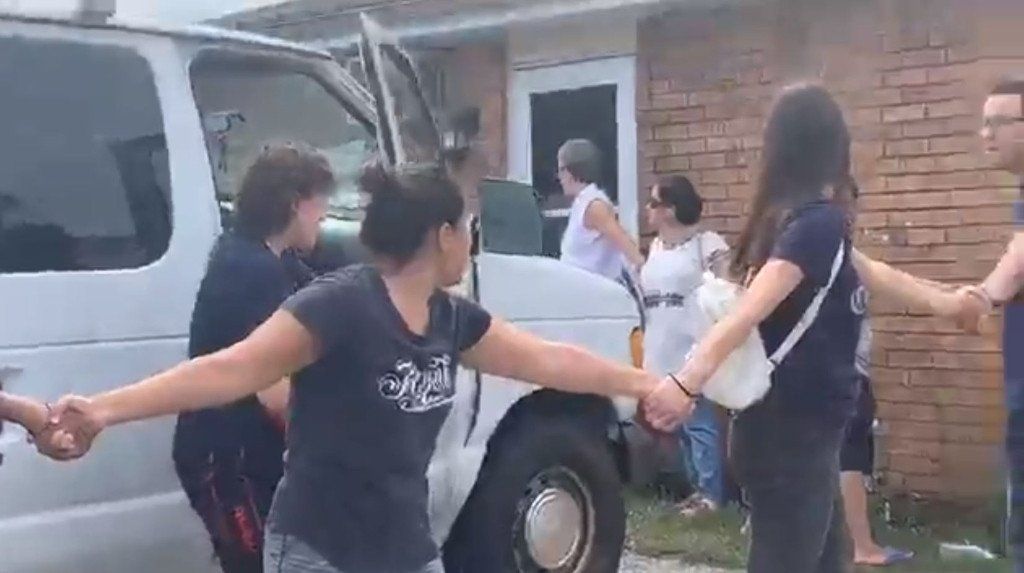 A group of people are holding hands in front of a van.