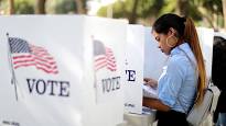 A woman is standing in front of a ballot box at a voting booth.