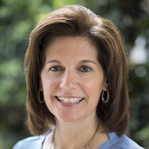 A woman wearing a blue shirt and earrings is smiling for the camera.
