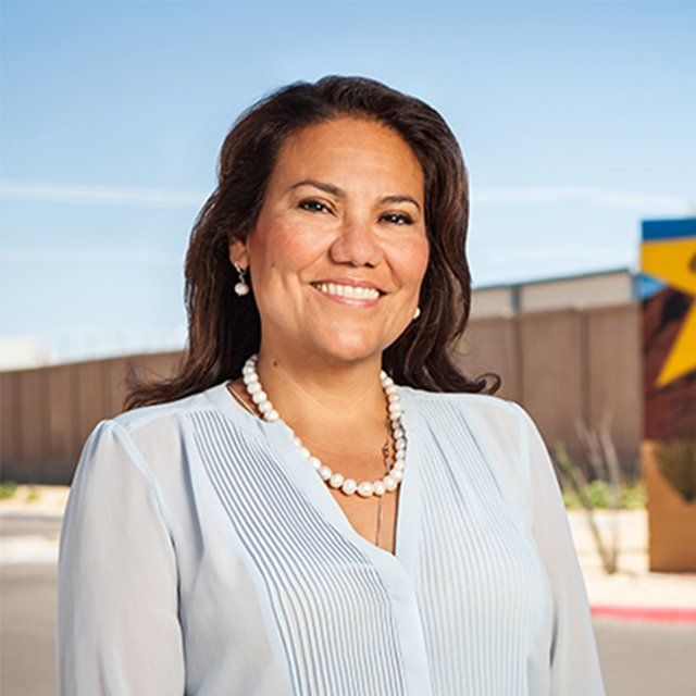 A woman wearing a pearl necklace and earrings is smiling for the camera.
