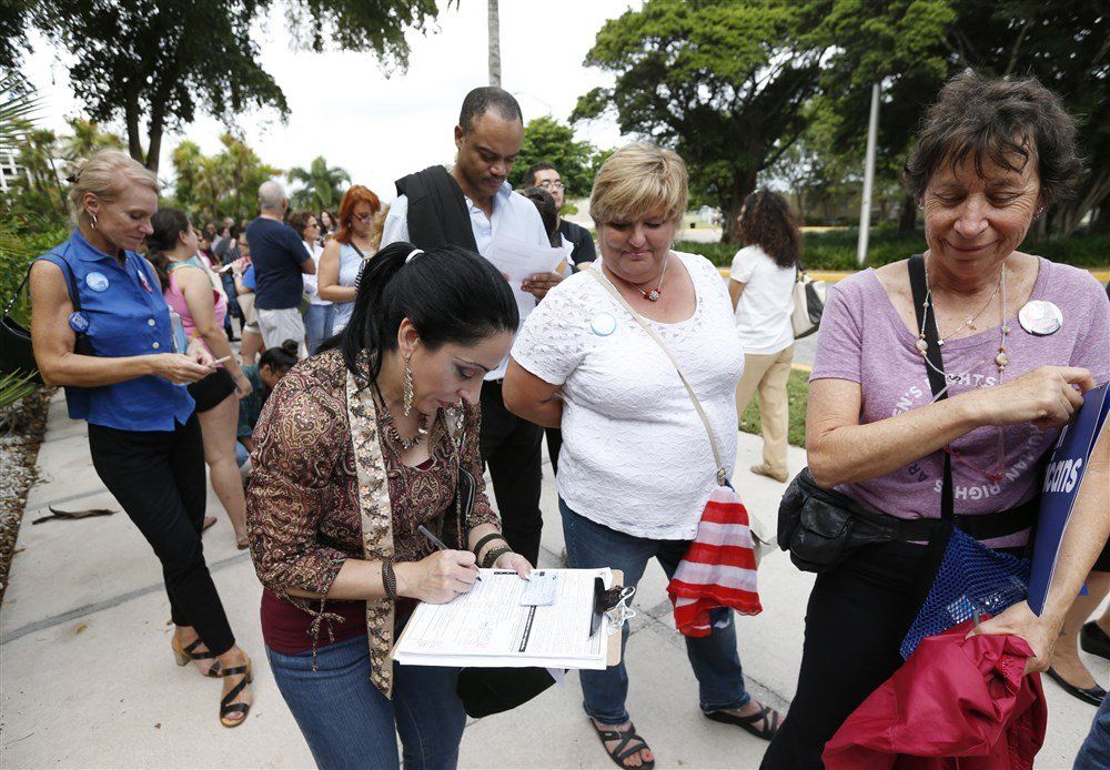 A group of people are standing on a sidewalk and one woman is writing on a clipboard