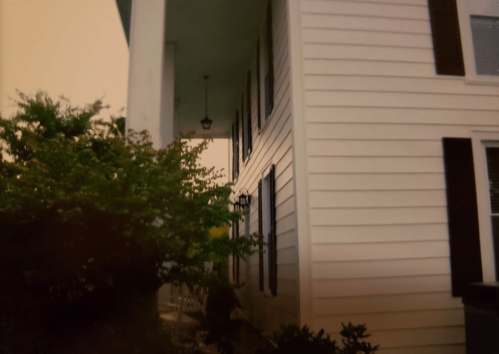 A white house with a porch and trees in front of it