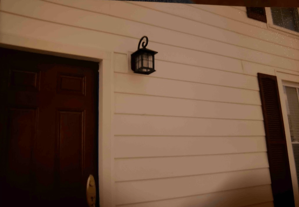 A white house with a brown door and a lantern on the side
