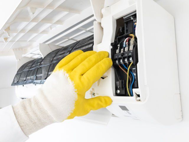 Person in yellow gloves opening an air conditioning unit for maintenance.