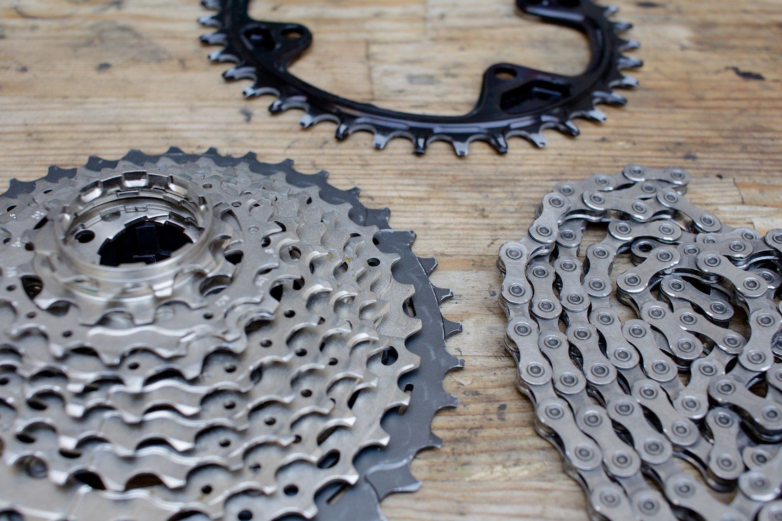Een close-up van een ketting, cassette en kettingblad op een houten tafel.