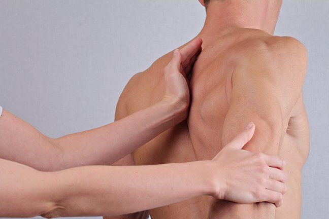 Man's back with another person's hands, one between his should blades, the other pulling his right arm back