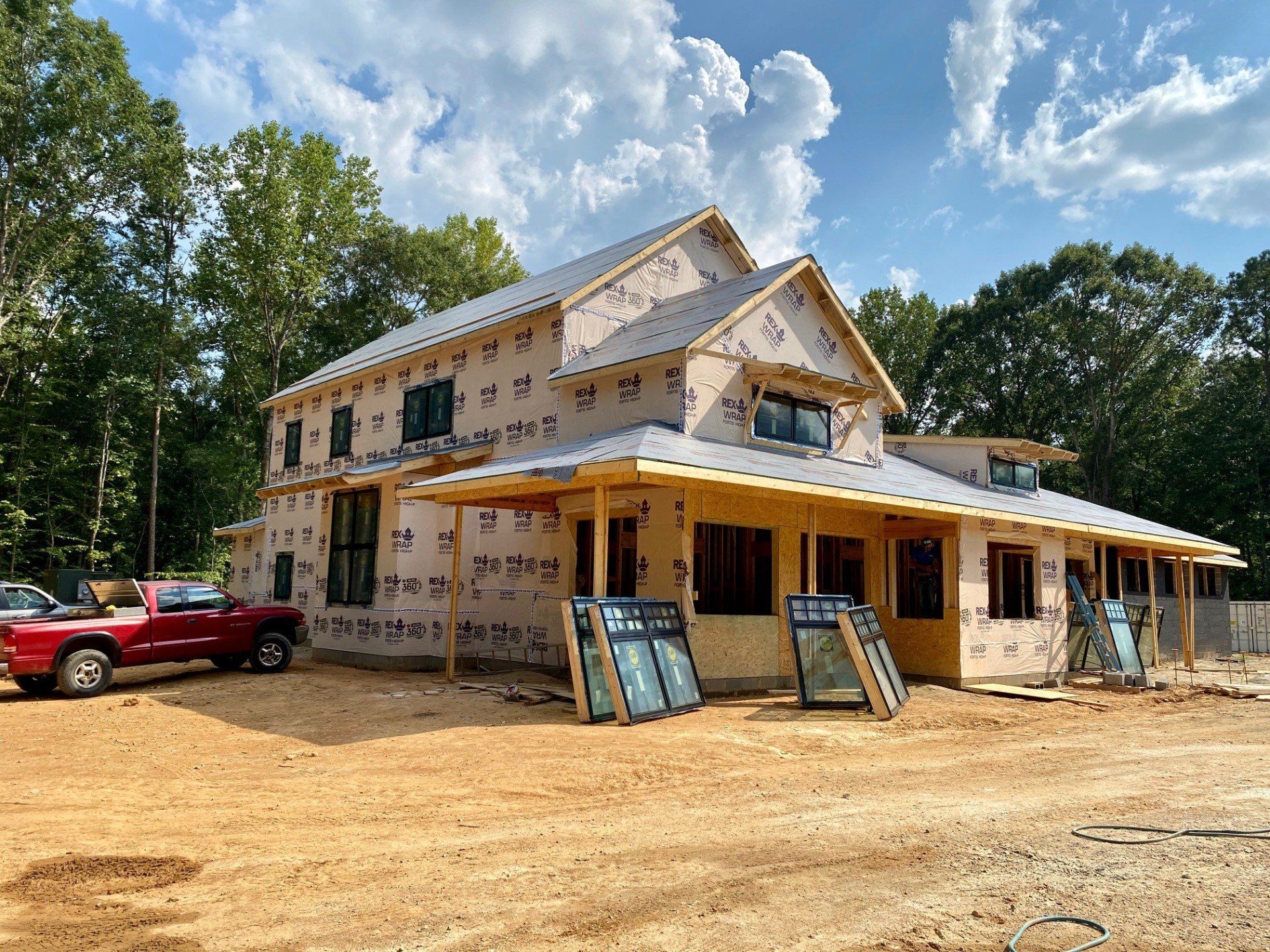 A red truck is parked in front of a house under construction.
