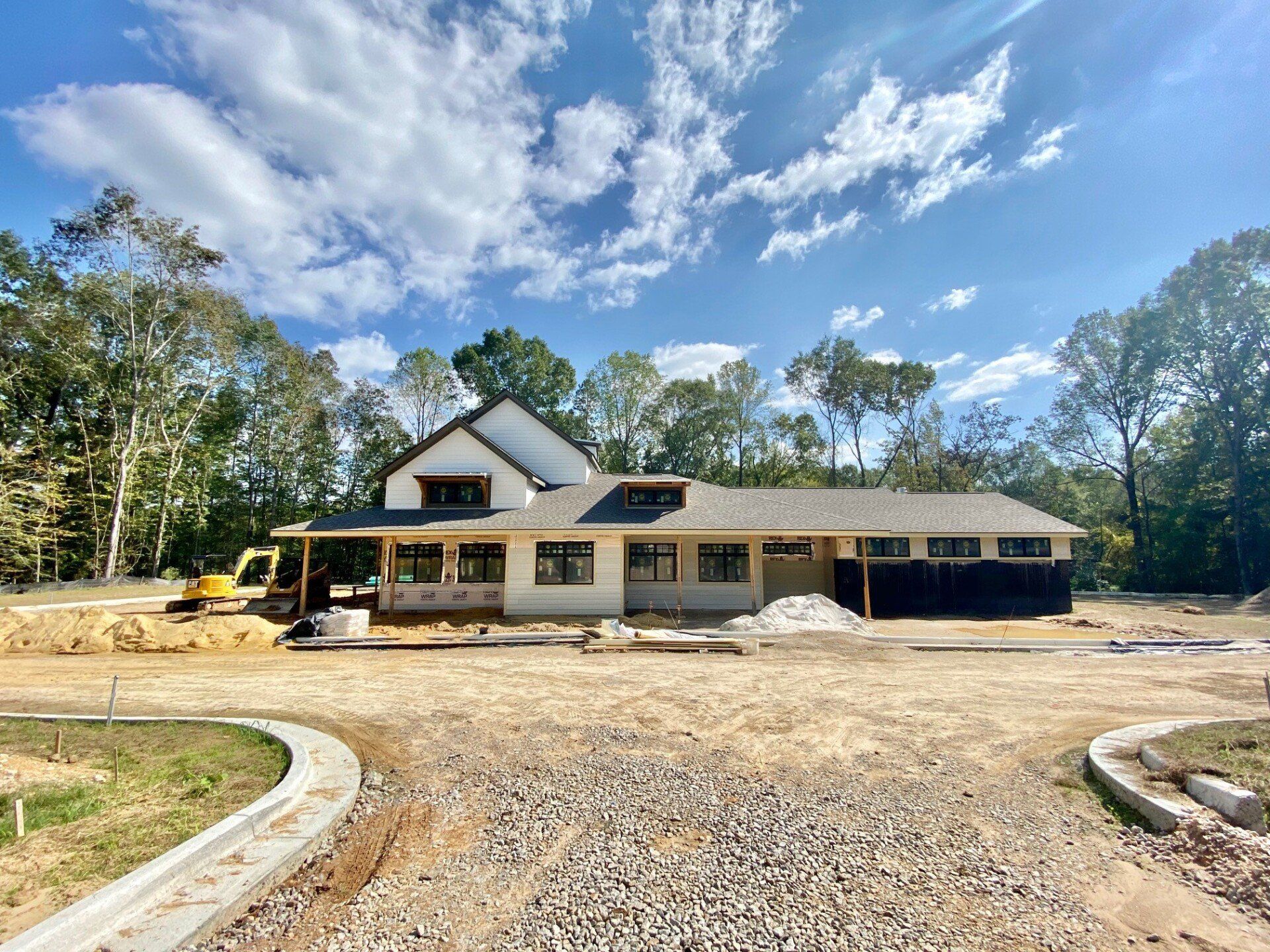 A large house is being built in a dirt lot surrounded by trees.
