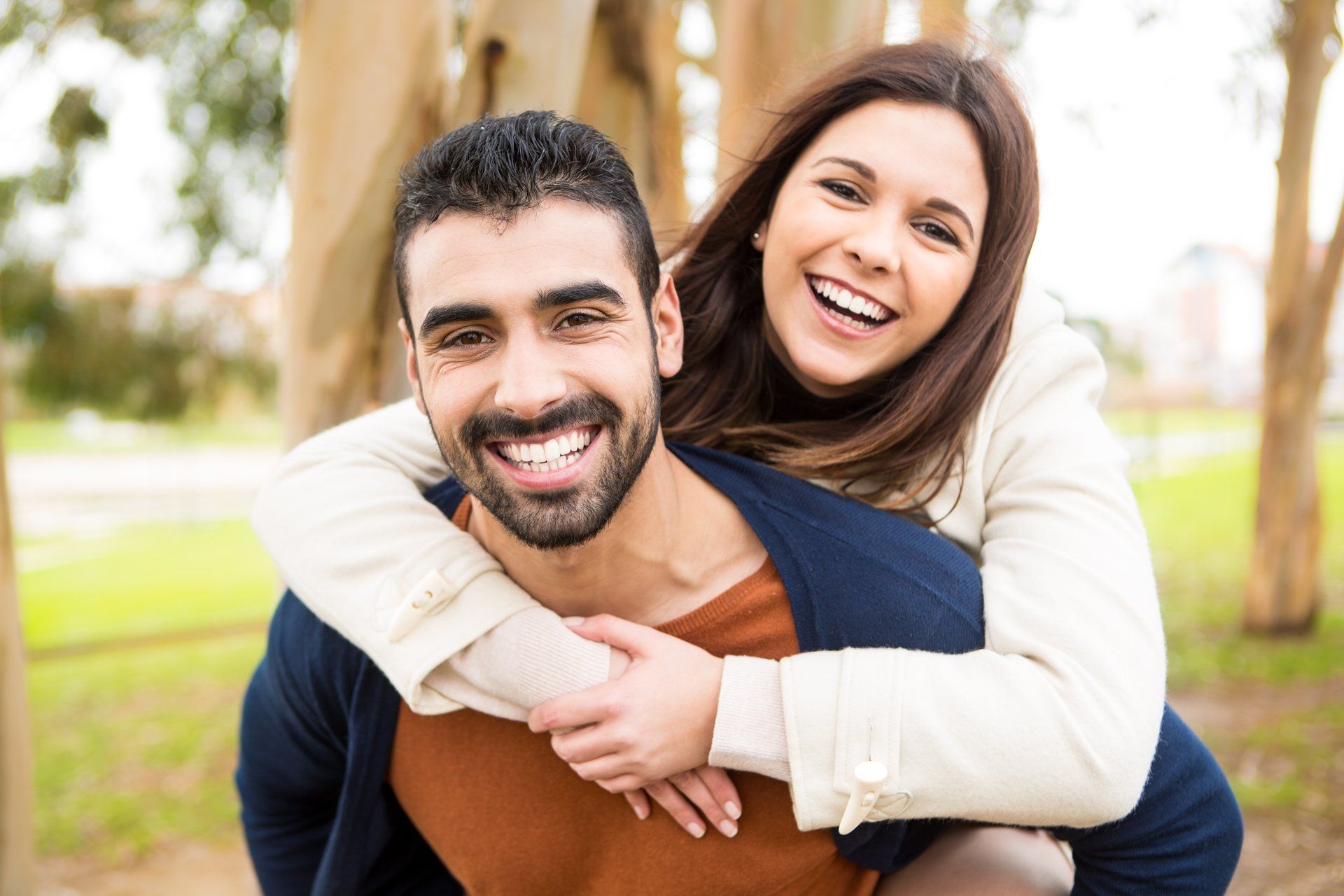 A man is carrying a woman on his back in a park.