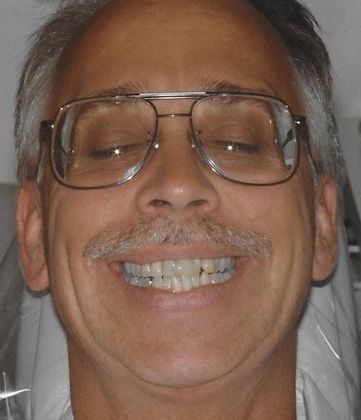 A man with glasses and a mustache is smiling with his eyes closed.