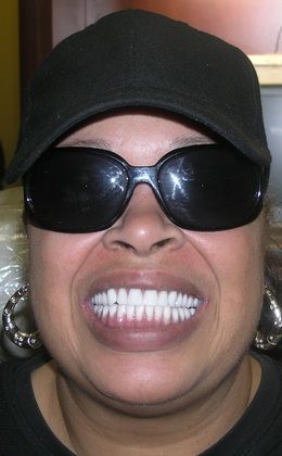 A woman wearing sunglasses and a hat is smiling.