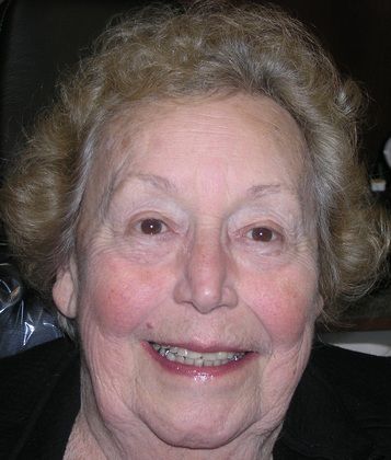 An elderly woman with braces on her teeth is smiling for the camera.