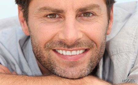 A man with a beard is smiling with his hand on his chin.