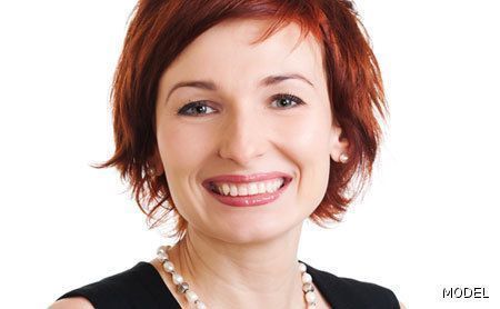 A woman with red hair is smiling and wearing a pearl necklace.