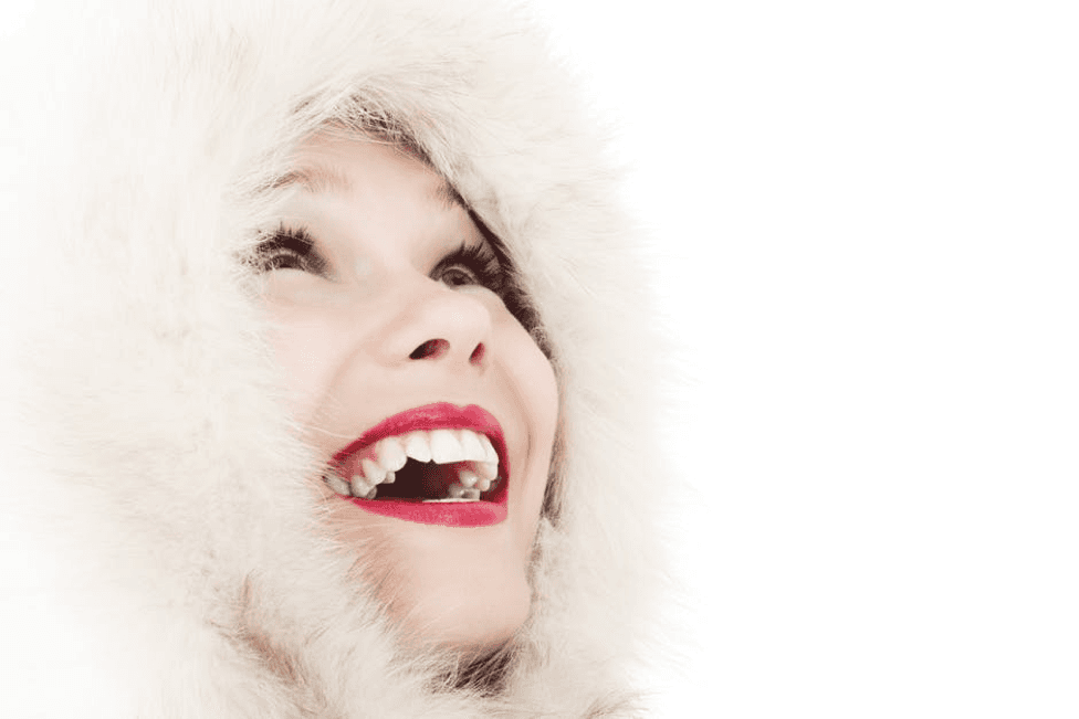 A woman wearing a fur hood is smiling with her mouth open.