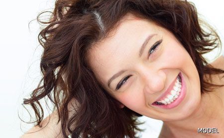 A woman with curly hair is smiling with her hand in her hair.