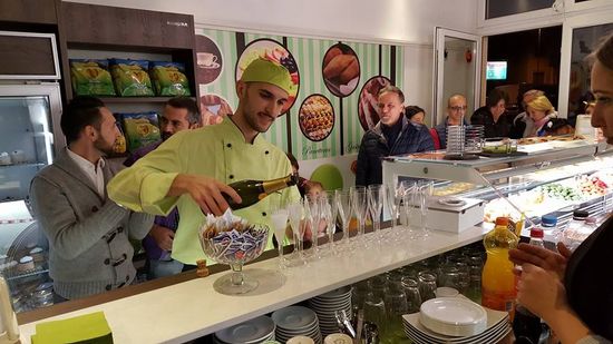 un barista che serve dello champagne dentro a dei bicchieri e delle persone attorno
