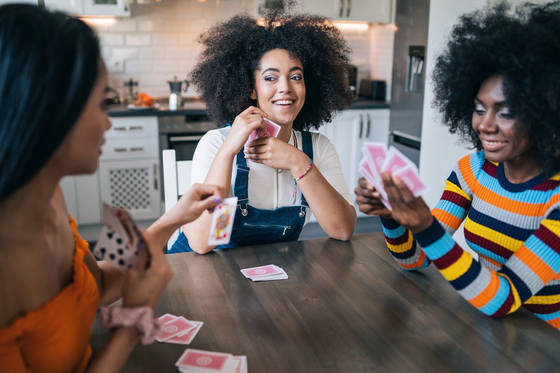 three women are sitting at a table playing cards .