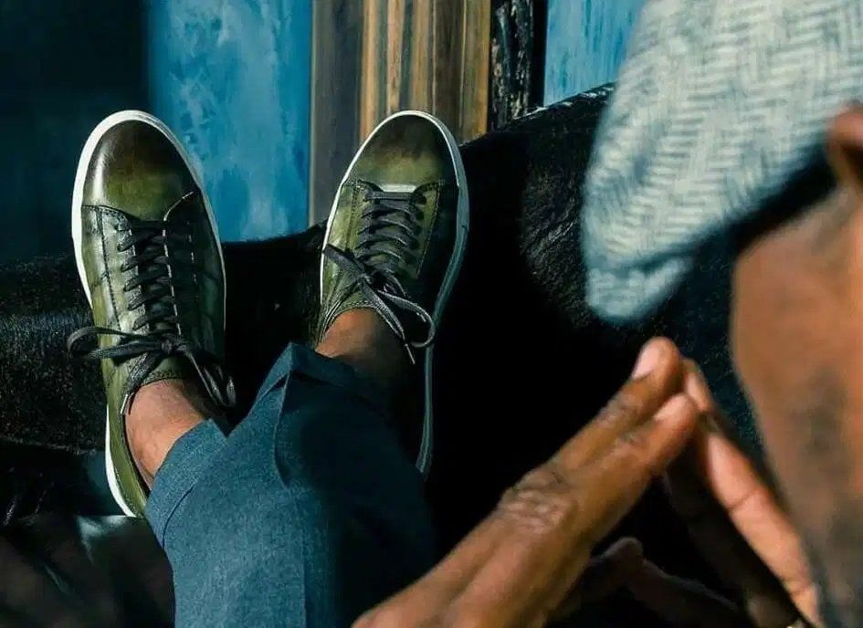 a man wearing a hat and sunglasses is sitting on a couch with his feet up .
