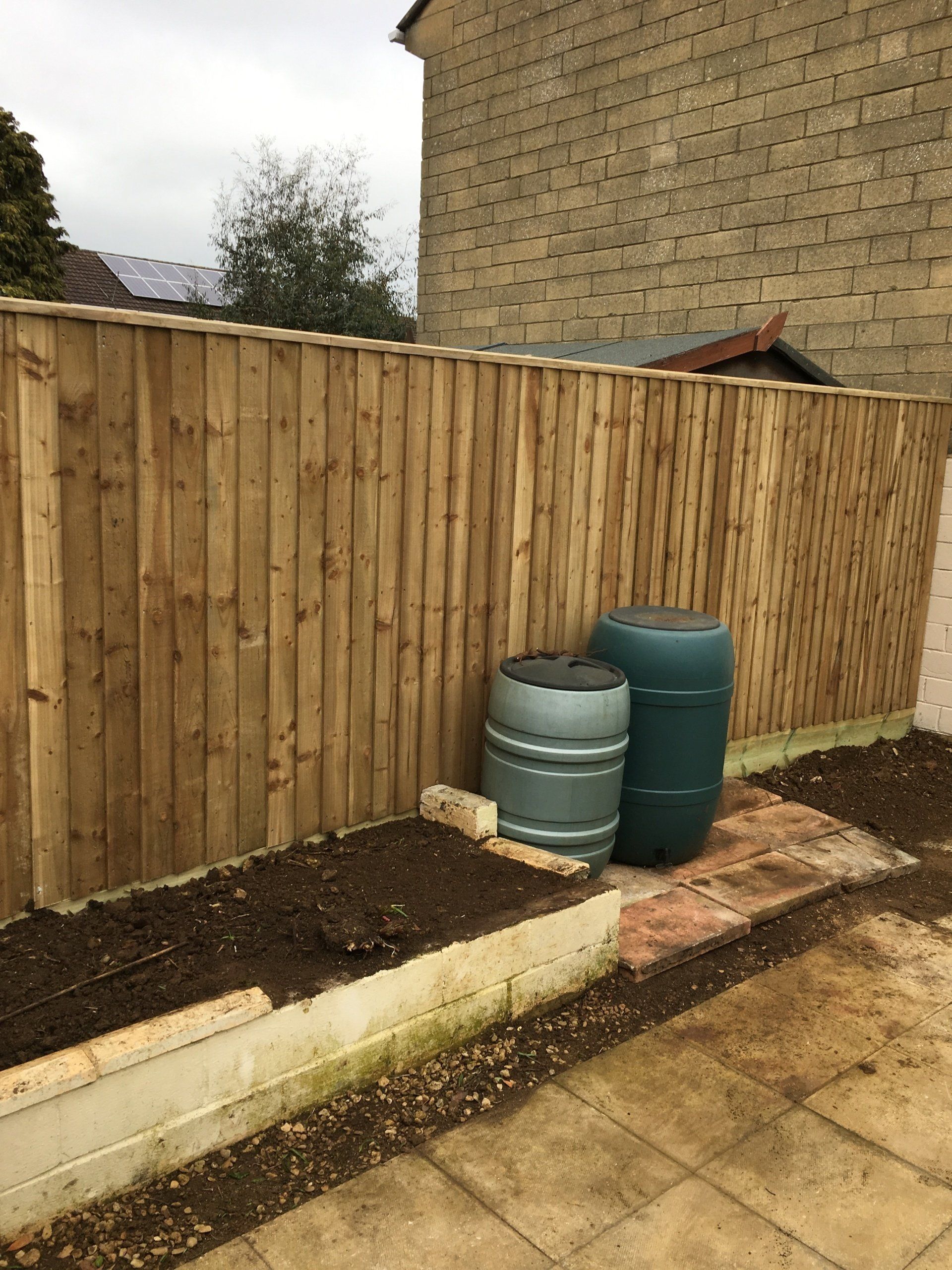 A wooden fence with two barrels in front of it.