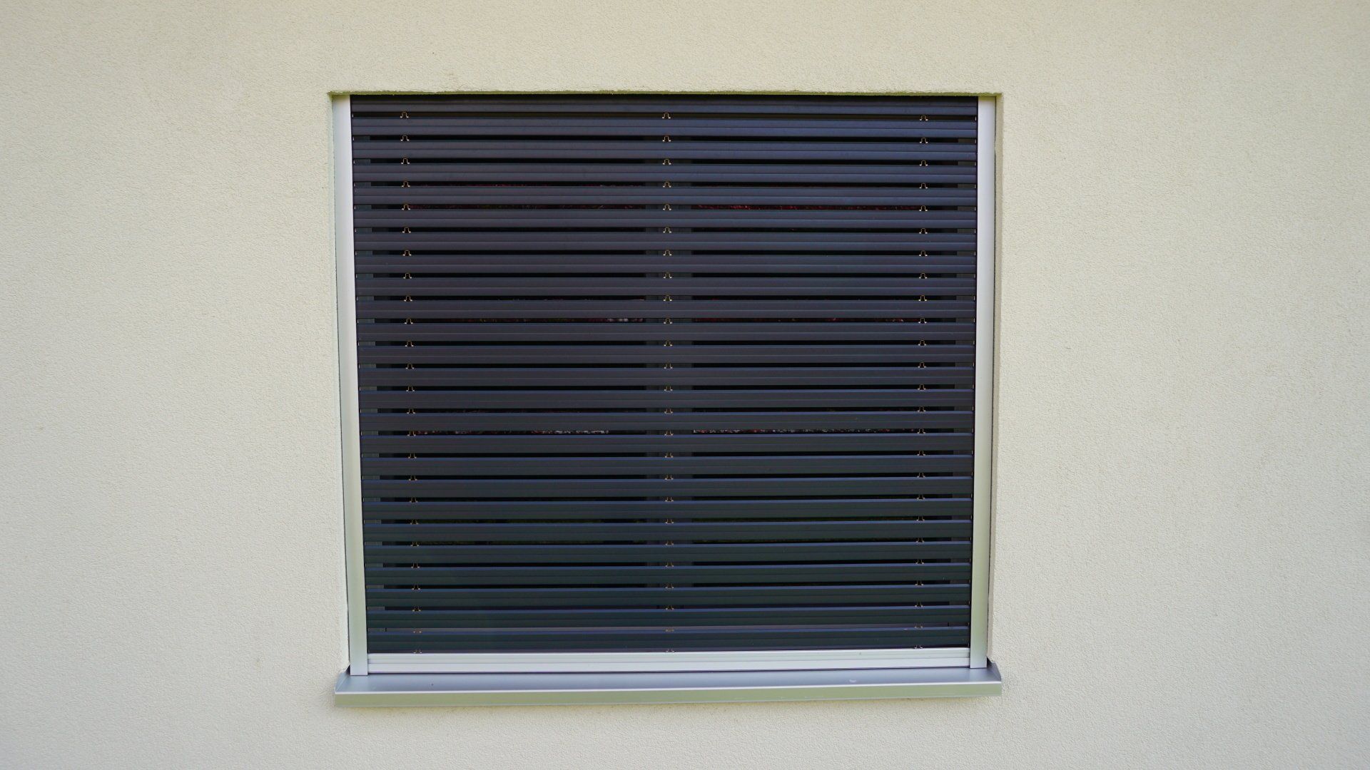 Une fenêtre avec un store noir dessus se trouve sur un mur blanc.