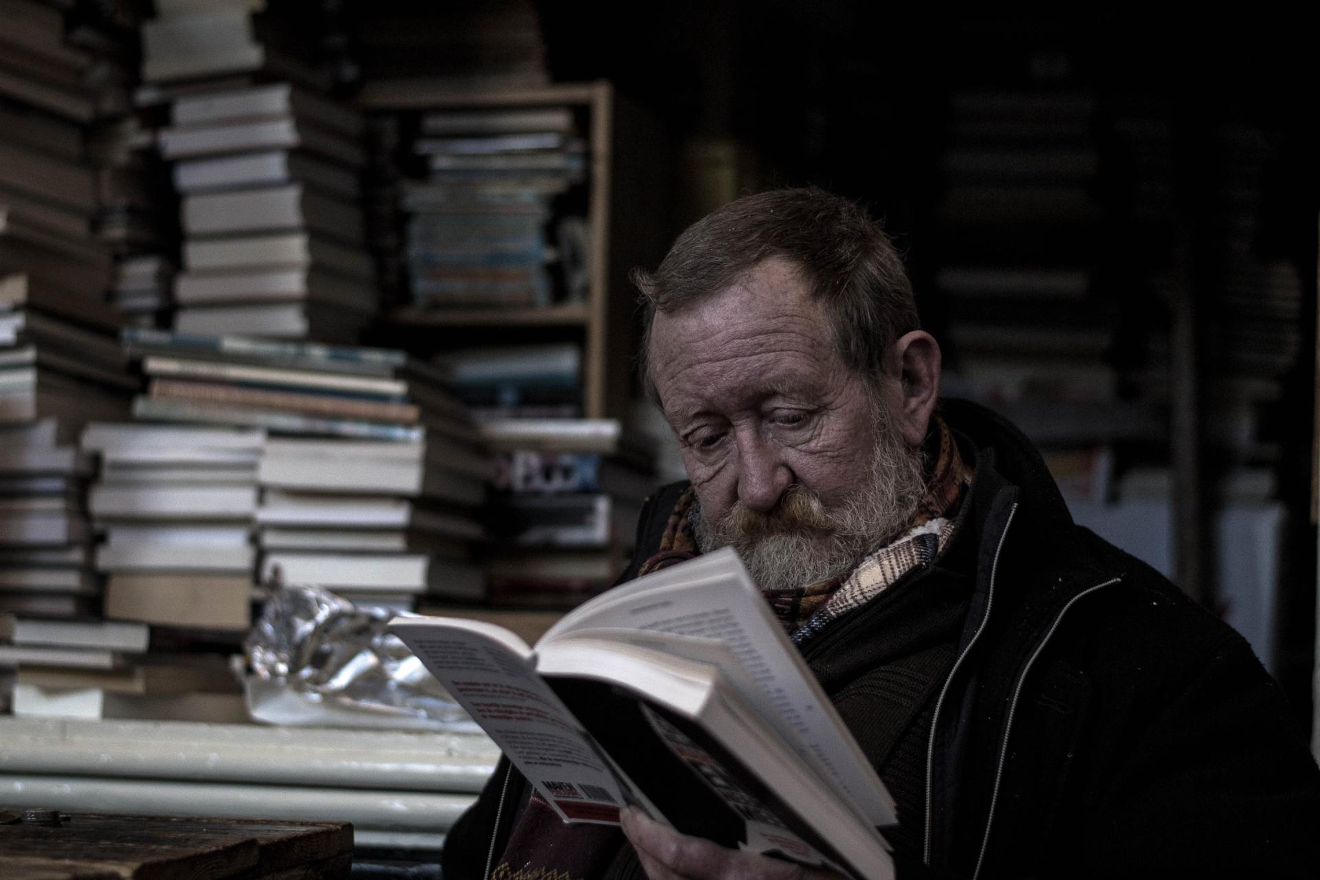 A man with a beard is reading a book in a library.
