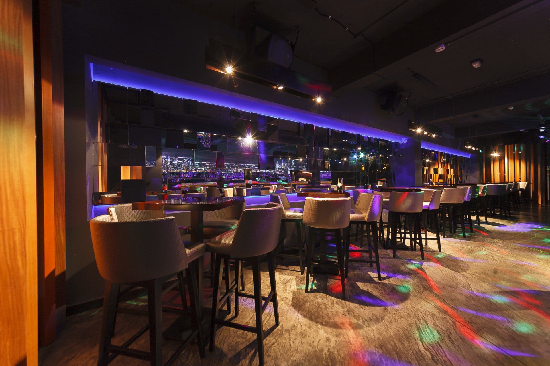 Un bar con mesas y sillas y luces moradas en el suelo.