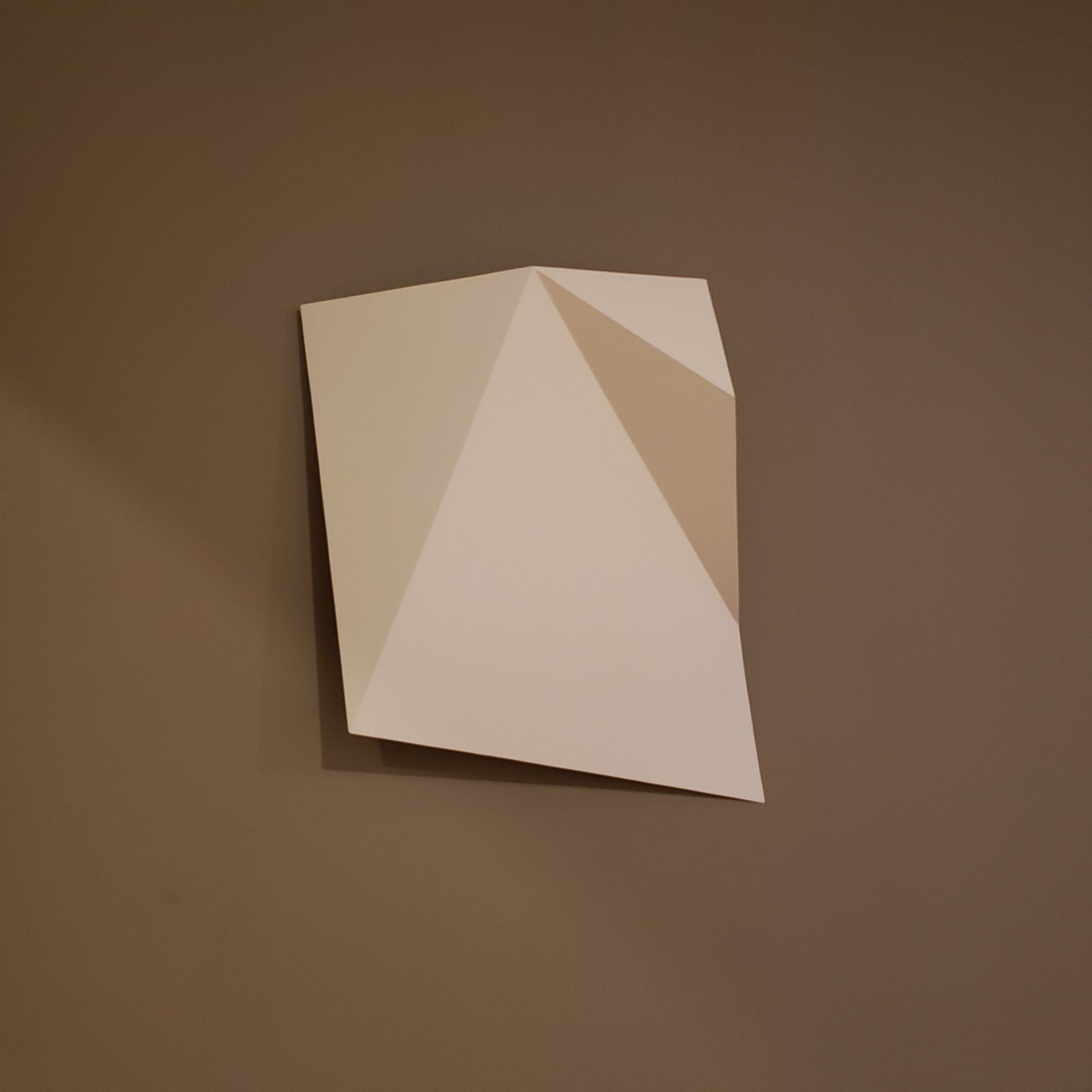 Un trozo de papel que parece una pirámide está colgado en una pared marrón.