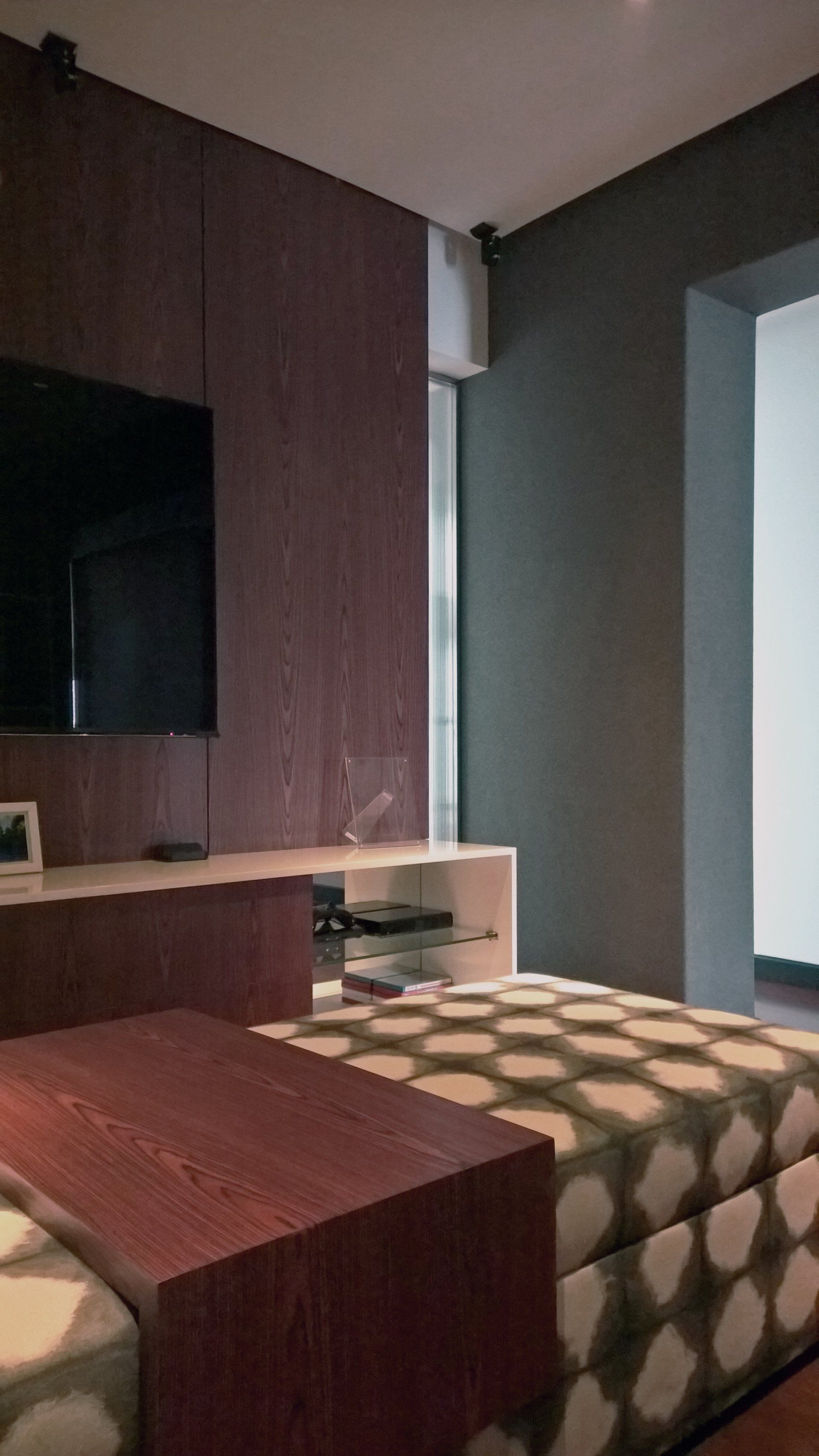 Una sala de estar con una cama, una mesa, una televisión y una ventana.