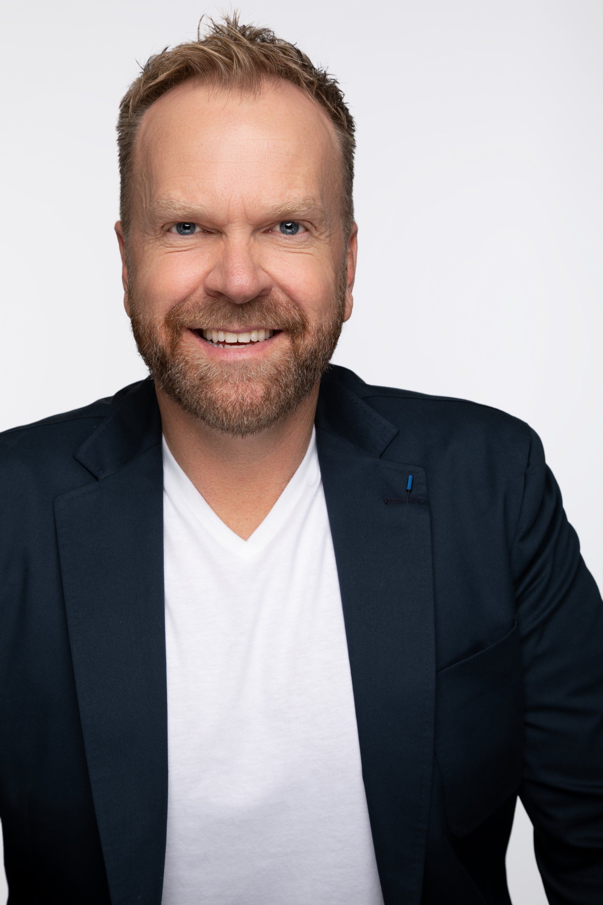 A man with a beard is wearing a blue jacket and a white shirt.