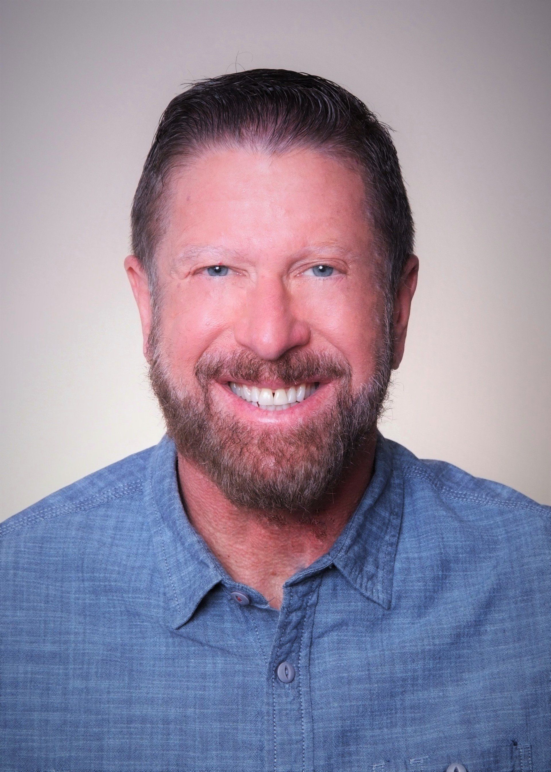 A man with a beard and a blue shirt is smiling for the camera.
