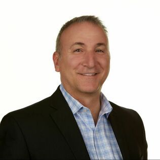 A man in a suit and plaid shirt is smiling for the camera.