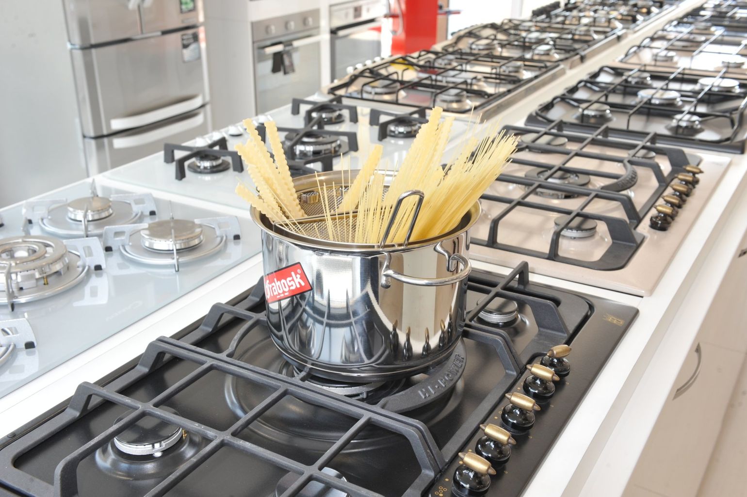 In uno showroom di elettrodomestici, una pentola in acciaio inossidabile piena di pasta cruda è appoggiata su un piano cottura a gas nero.