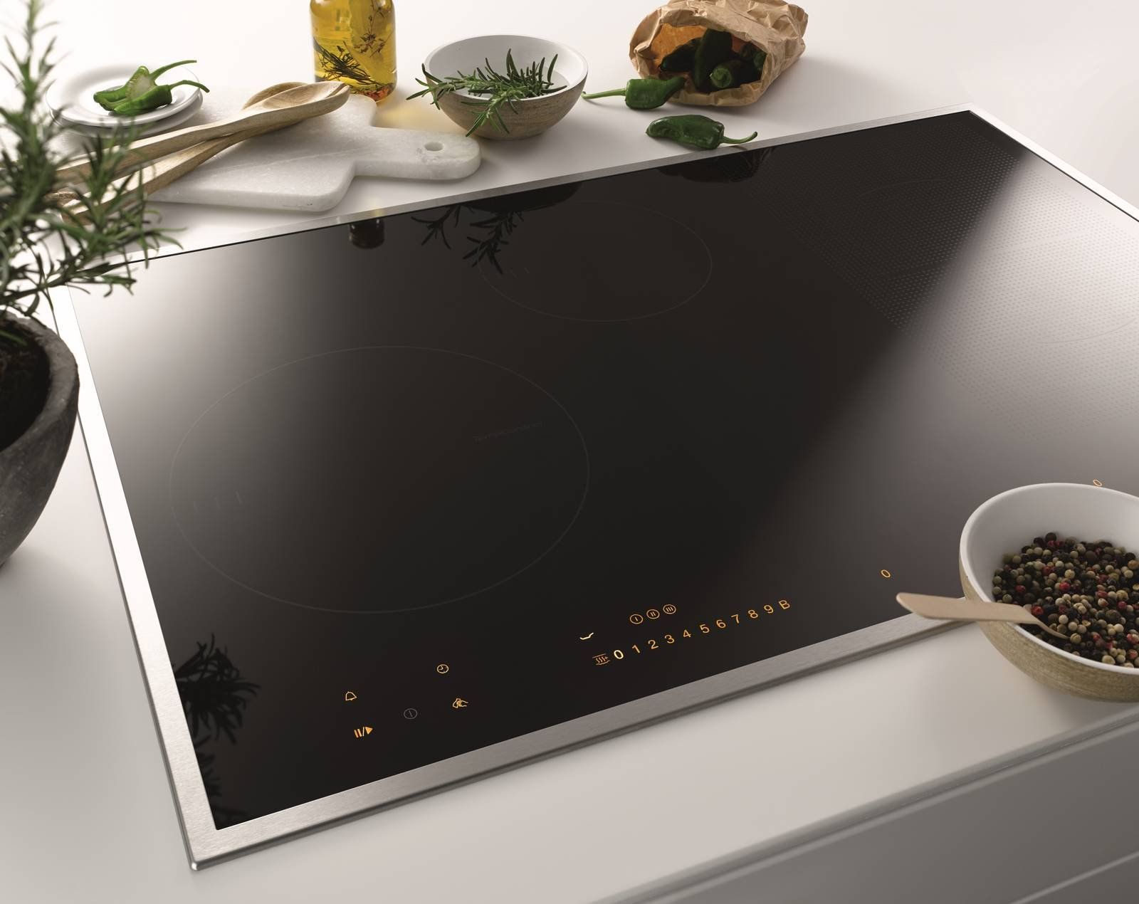 Un elegante piano cottura a induzione in vetro nero con comandi touch illuminati, posizionato su un bancone da cucina bianco con erbe aromatiche.