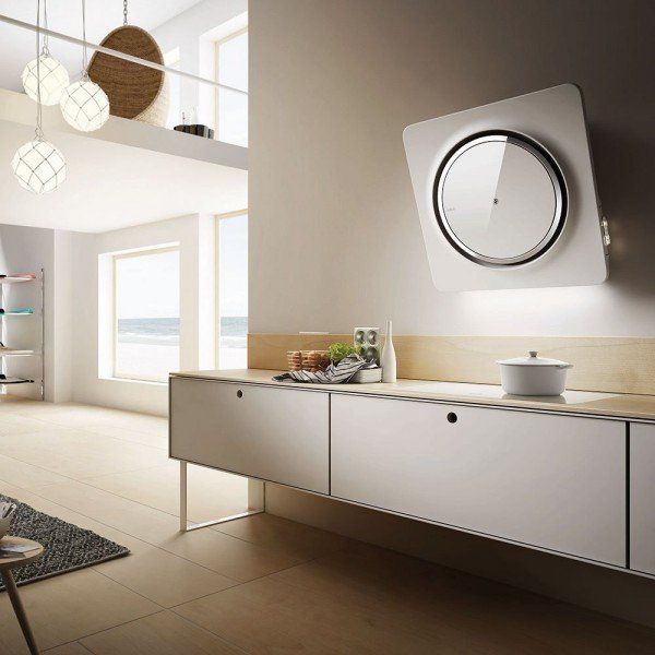 Un interno cucina moderno con una cappa aspirante minimalista bianca a parete, mobili chiari ed eleganti lampade a sospensione.