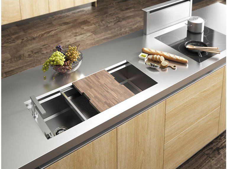 Un'isola cucina moderna con piano di lavoro in metallo, lavello in acciaio inox con tagliere in legno e piano cottura integrato.