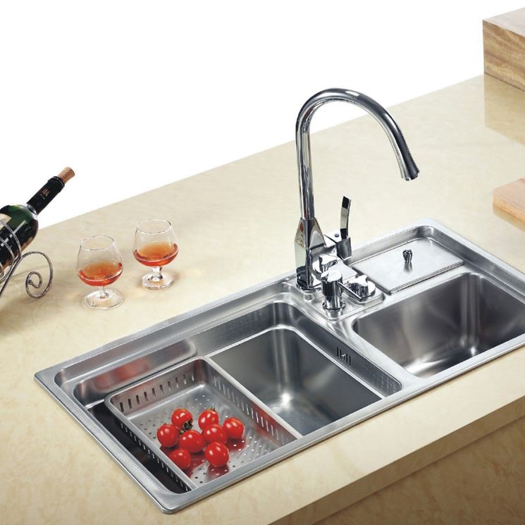 Un lavello da cucina in acciaio inox con rubinetto ad arco alto, scolapasta integrato per pomodori rossi e un piccolo coperchio in metallo.