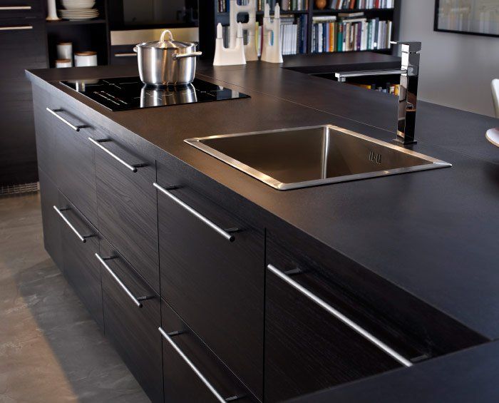 Un'isola cucina moderna con mobili in legno scuro, piano di lavoro nero, lavello in acciaio inox e piano cottura.