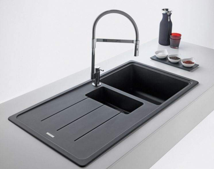 Un lavello da cucina grigio scuro con scolapiatti, una piccola vasca di preparazione e un rubinetto alto cromato su un piano di lavoro bianco.
