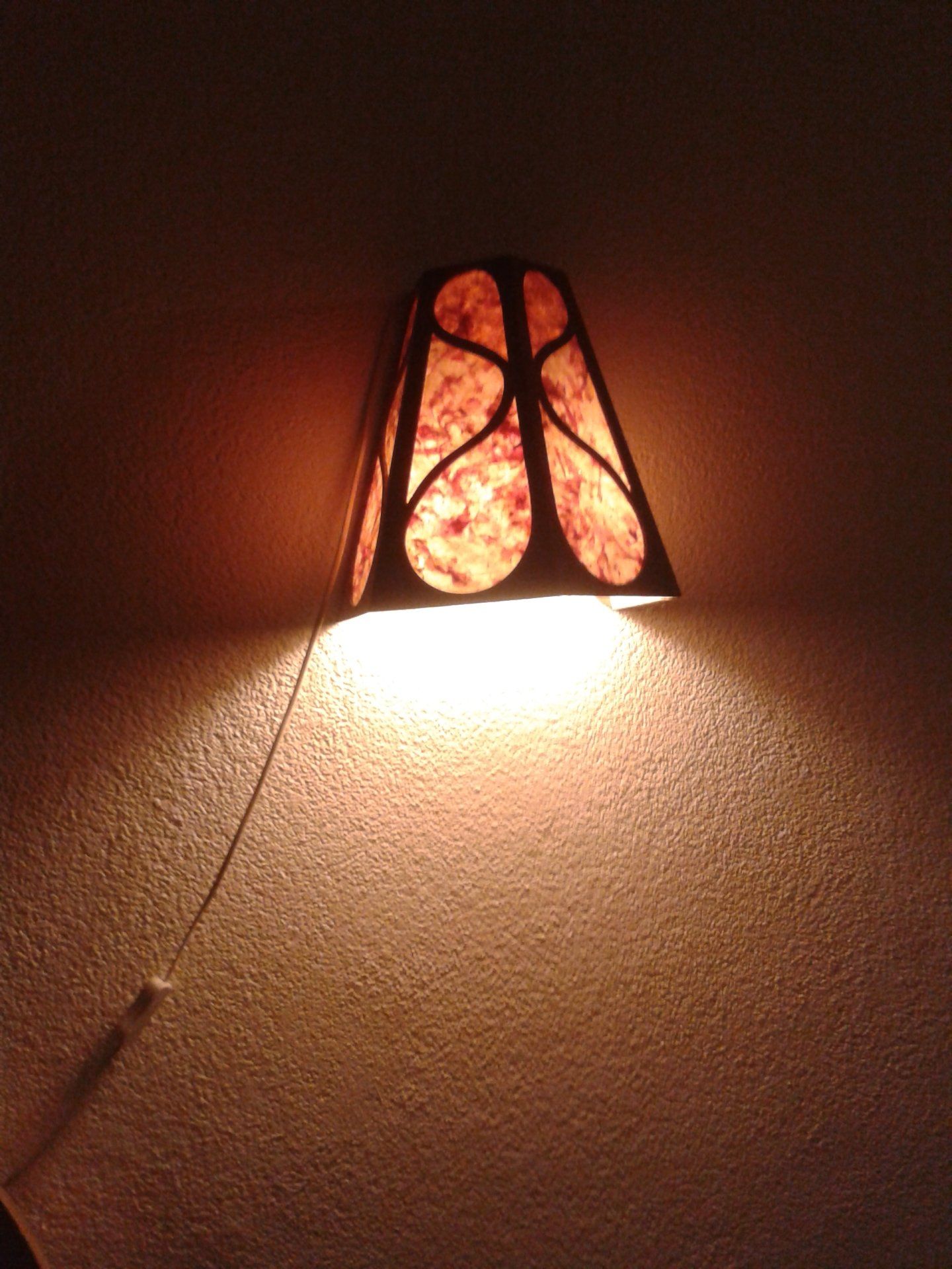 Wandlamp met een warme oranje kap die licht werpt op een muur met structuur.