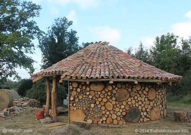 Kleine ronde stenen hut met een pannendak in een landelijke buitenomgeving, omgeven door bomen en groen.