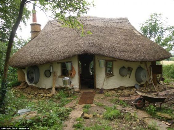 Een huisje voor 600 euro. met een rieten dak, ronde ramen en een smal stenen pad in een lommerrijke tuin.