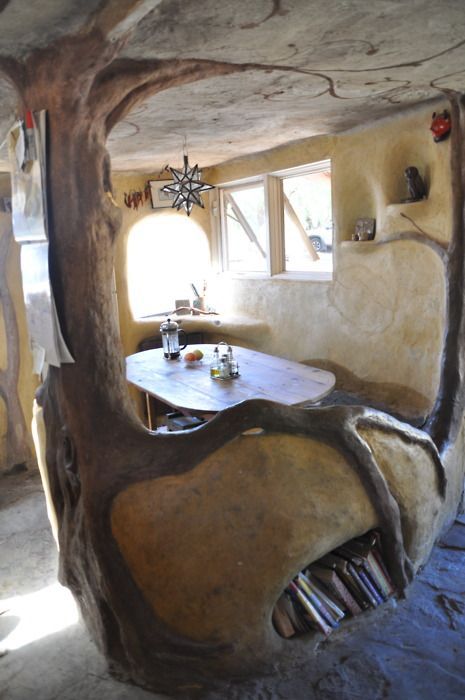 Rustieke kamer met een houten tafel, stoelen, raam en boekenkasten ingebouwd in gebogen lemen muren.