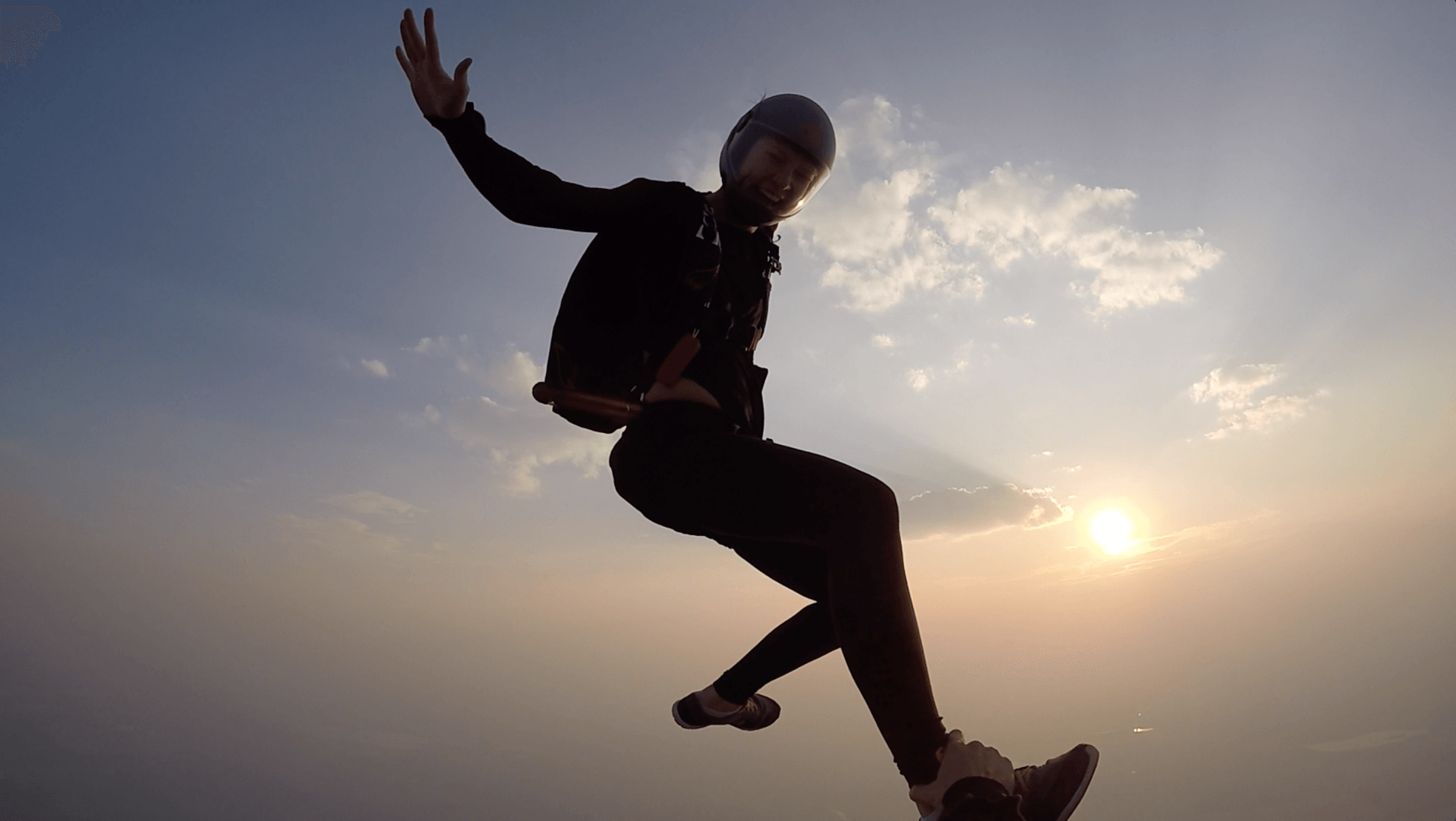 A man is jumping in the air with a parachute at sunset.