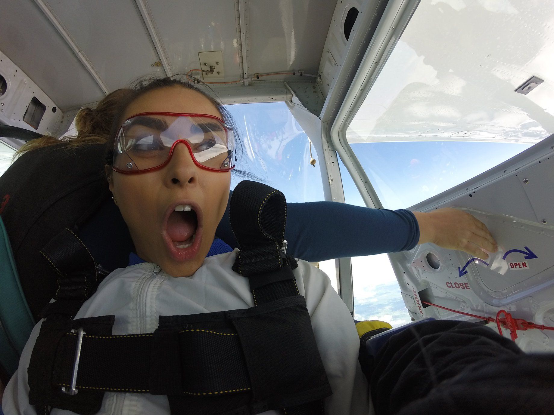 A woman wearing glasses is sitting in a plane with her mouth open.