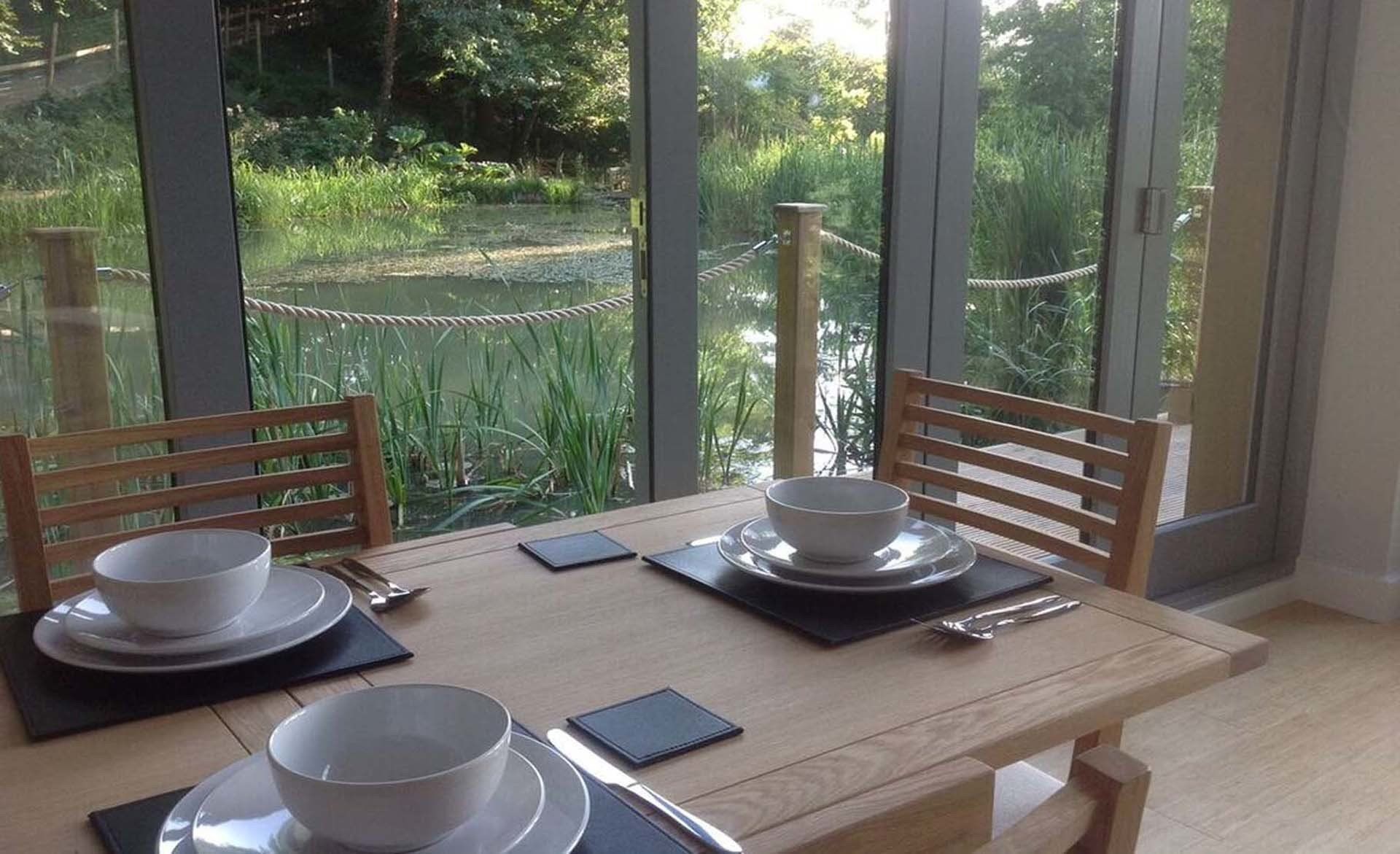 a Table is set for dining with bi fold doors open to a small lake