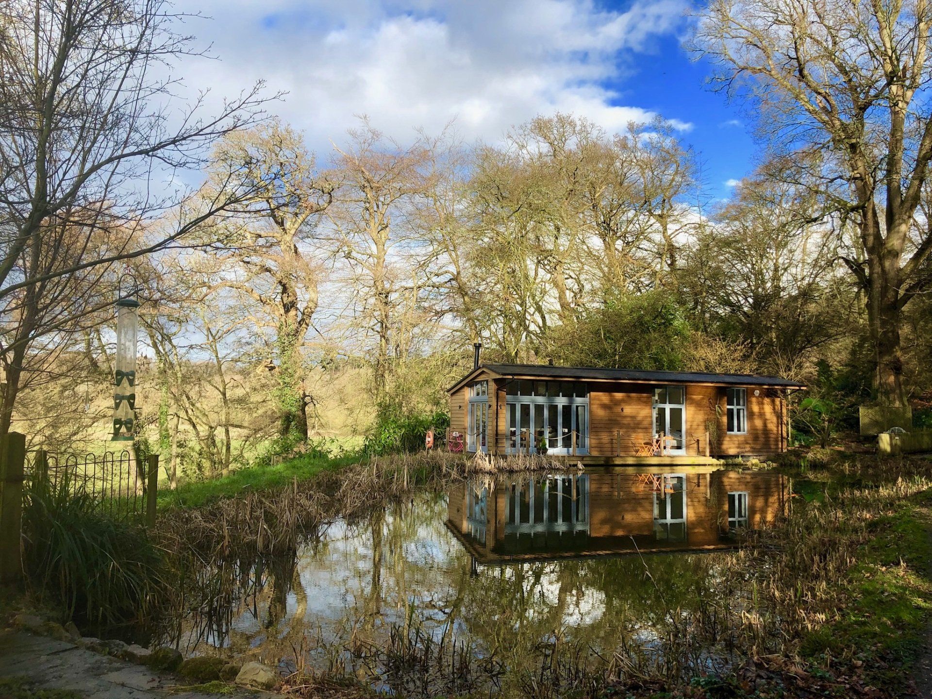 A cedar clad woodland Lodge is reflected on the lake it sits upon in a woodland setting