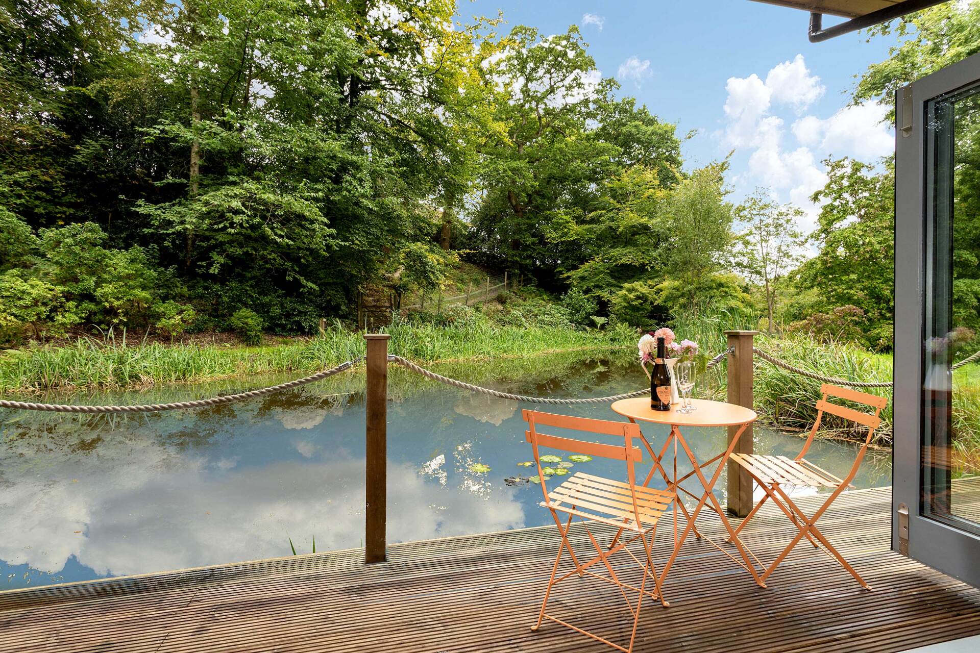 a table with a bottle of prosecco and 2 glasses  on a verandah overlooking a lake